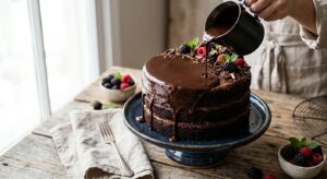 A high-angle, professional editorial shot of a decadent chocolate cake being drizzled with a smooth,